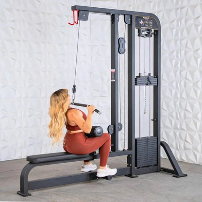 Woman performing lat pulldown exercise on a black selectorized cable machine with dual weight stacks and padded seat in a gym setting.