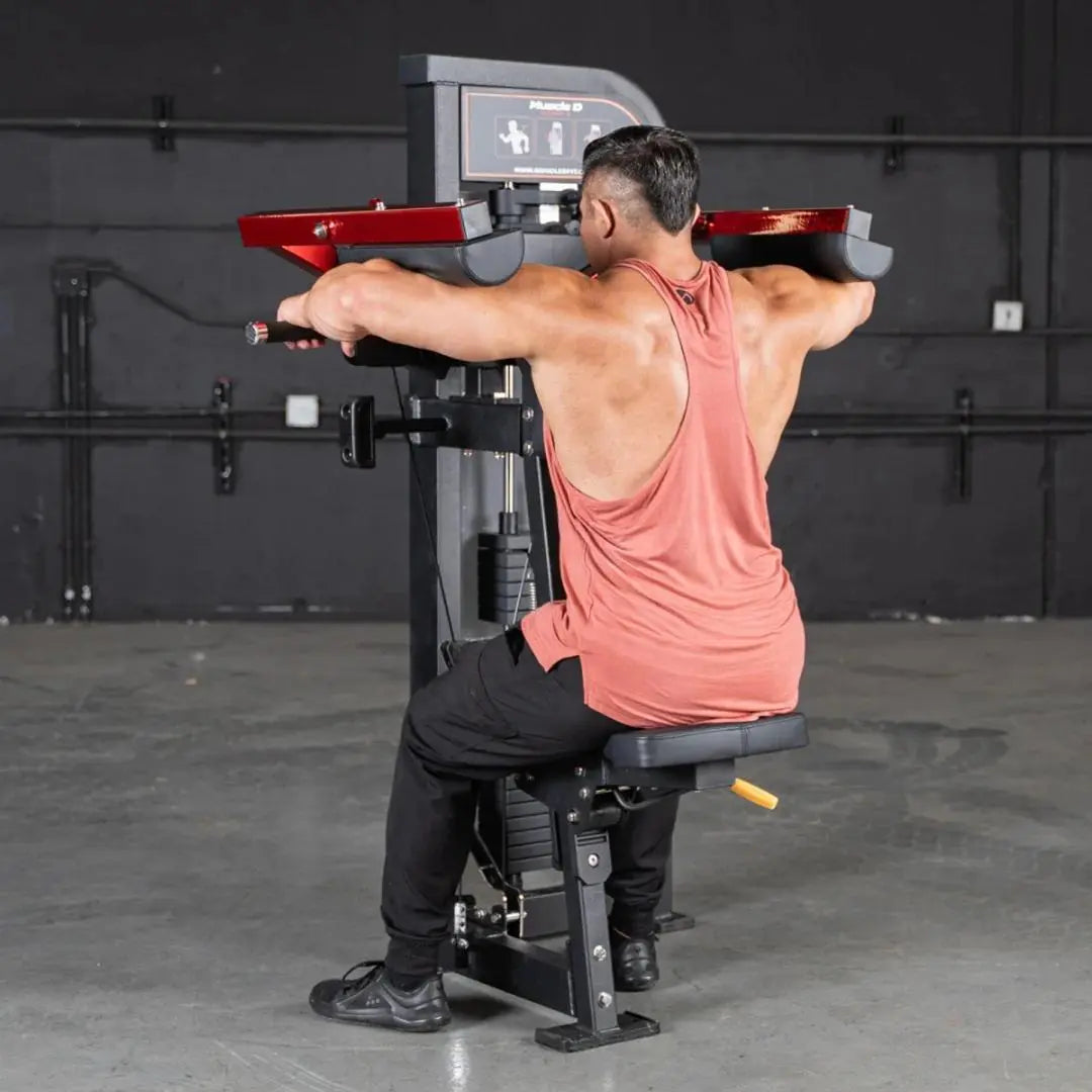 Man performing lateral raise on a black and red selectorized machine with padded red handles in a commercial gym setting.
