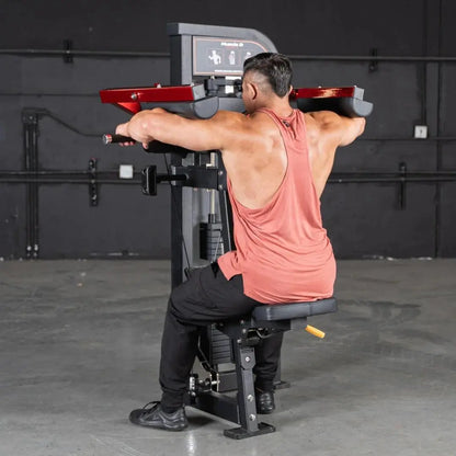 Man performing lateral raise on a black and red selectorized machine with padded red handles in a commercial gym setting.