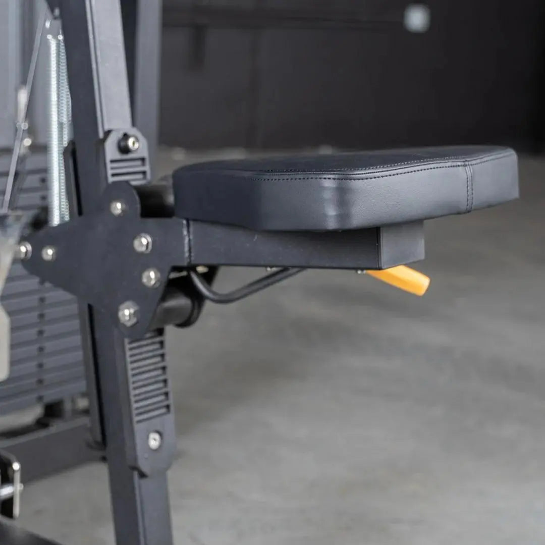 Close-up of a selectorized lateral raise machine showing the gray padded arm rest and black metal frame with adjustment bolts and yellow selector pin in a gym setting.