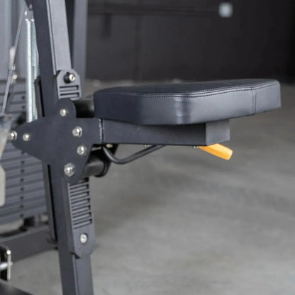 Close-up of a selectorized lateral raise machine showing the gray padded arm rest and black metal frame with adjustment bolts and yellow selector pin in a gym setting.