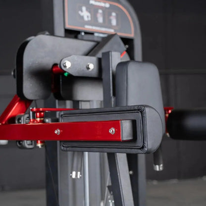 Close-up of lateral raise machine showing padded gray and red arm lever with black grip pad and control panel above against dark background.