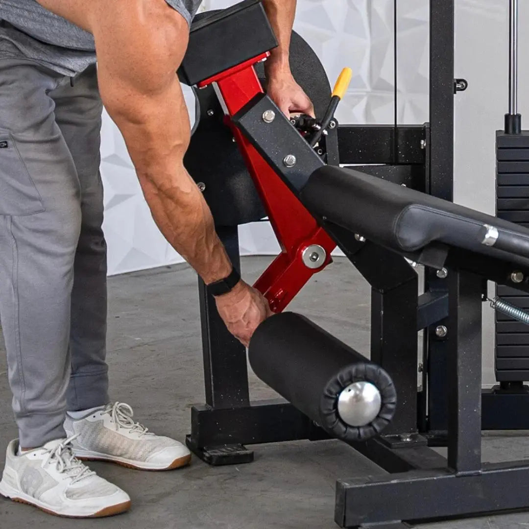 Man performing leg extension on a selectorized machine with red and black frame, padded leg rest, and metal weight stack selector lever in a gym setting.