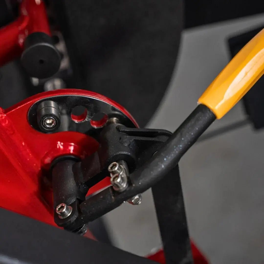 Close-up of red and black leg extension machine pivot joint with yellow and black handle attachment and metal adjustment bolts.