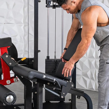 Man performing leg extension on a black selectorized leg extension machine with red accents in a gym setting with white textured wall backdrop.