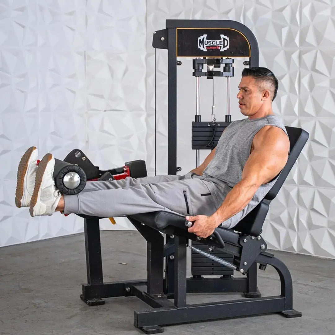 Man performing a leg extension exercise on a black Muscle D selectorized leg extension machine with weight stack, against a white textured wall.