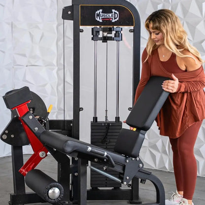 Woman performing leg extension on a black and red Muscle D Fitness selectorized leg extension machine with padded seat and footrest in a studio setting.