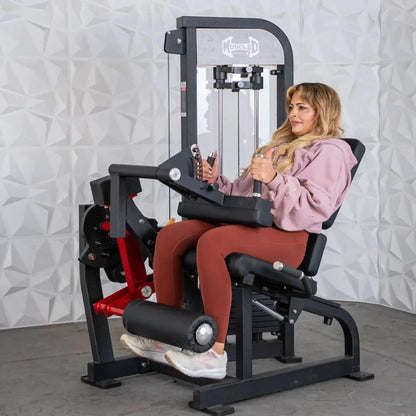 Woman performing a seated leg extension exercise on a black and red commercial leg extension and curl combo machine with a white textured wall background.