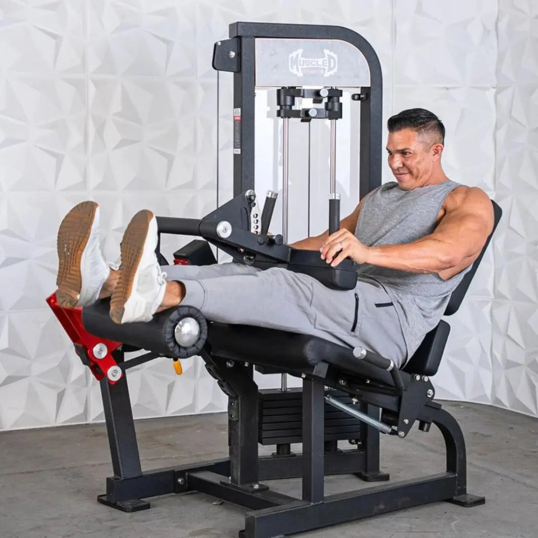 Man performing seated leg extension and curl on a black commercial leg extension and curl combo machine with red foot pads and white interior frame.