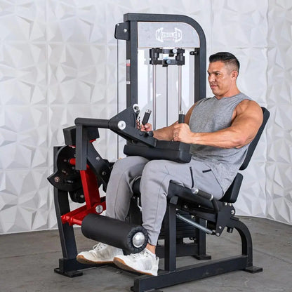 Man performing a seated leg curl on a black and red selectorized leg extension and curl combo machine with white textured wall backdrop.