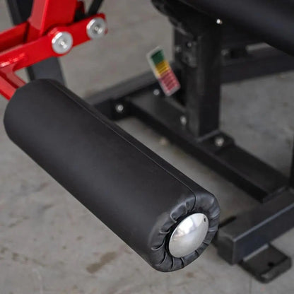 Black padded leg extension/curl machine seat with white adjustment knob, red frame arm visible above, and multicolor resistance indicator label on black frame.