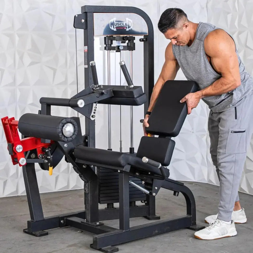 Man performing a seated leg curl on a black and red selectorized leg extension and curl combo machine with padded seat and backrest against a white textured backdrop.