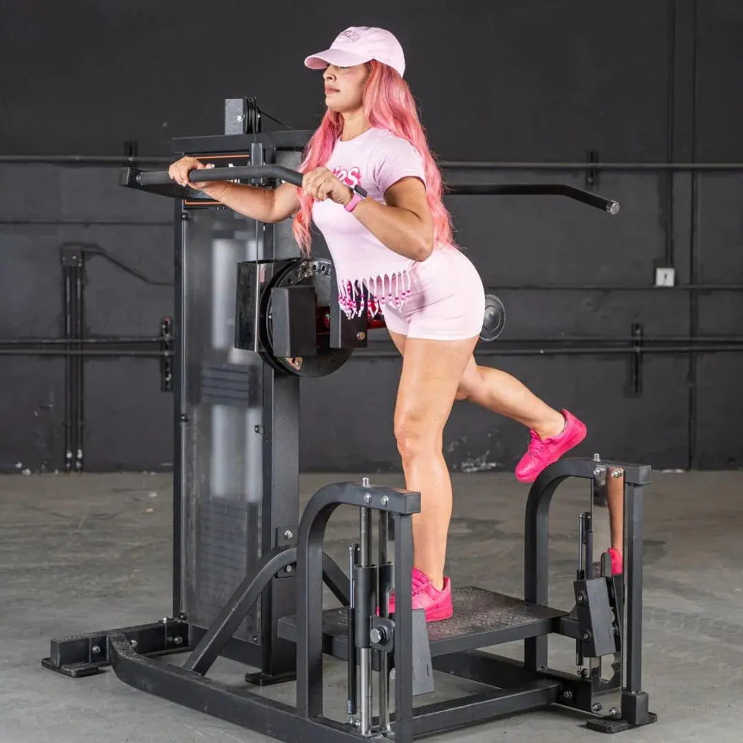 Woman performing hip thrust on a black selectorized multi-hip machine in a gym setting, wearing a white cap and pink athletic shoes.