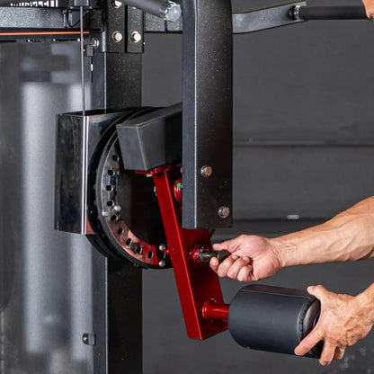 Person adjusting the red weight selector pin on a multi-hip machine with black speckled frame and black padding.