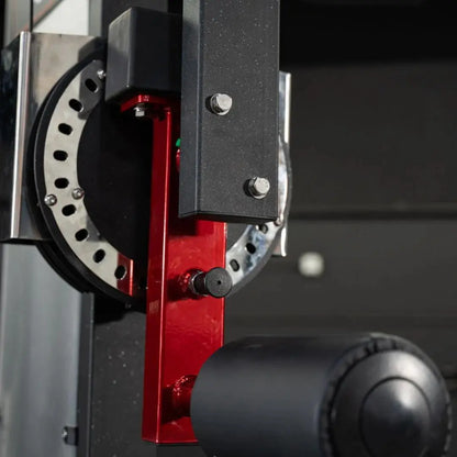 Close-up detail of a selectorized multi-hip machine showing the red metal frame, black textured side panel with adjustment bolts, white weight plate selector dial, and black cylindrical foot pad.