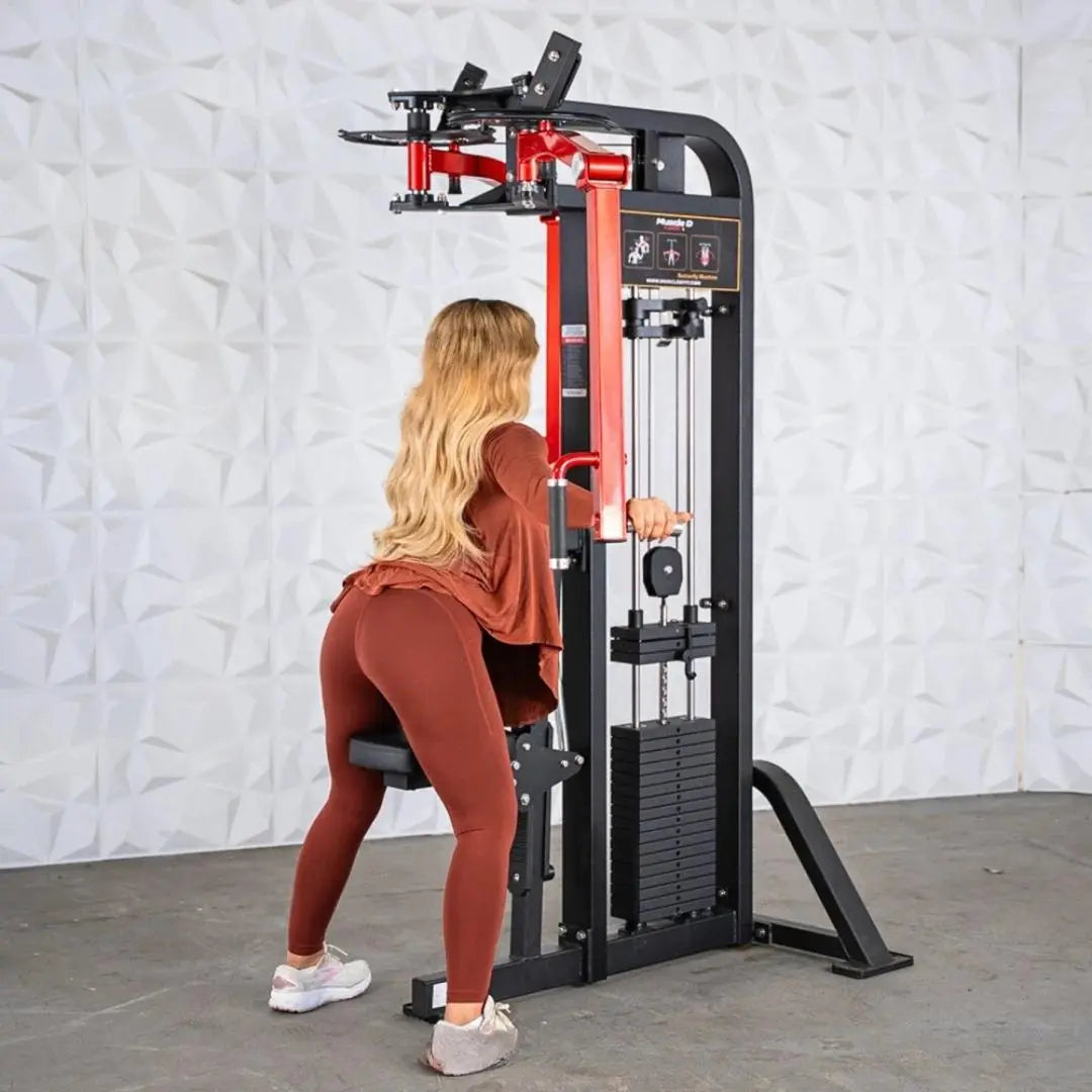 Woman performing pec and rear deltoid exercise on a selectorized combo machine with red and black frame, weight stack visible on the side, against white textured wall.