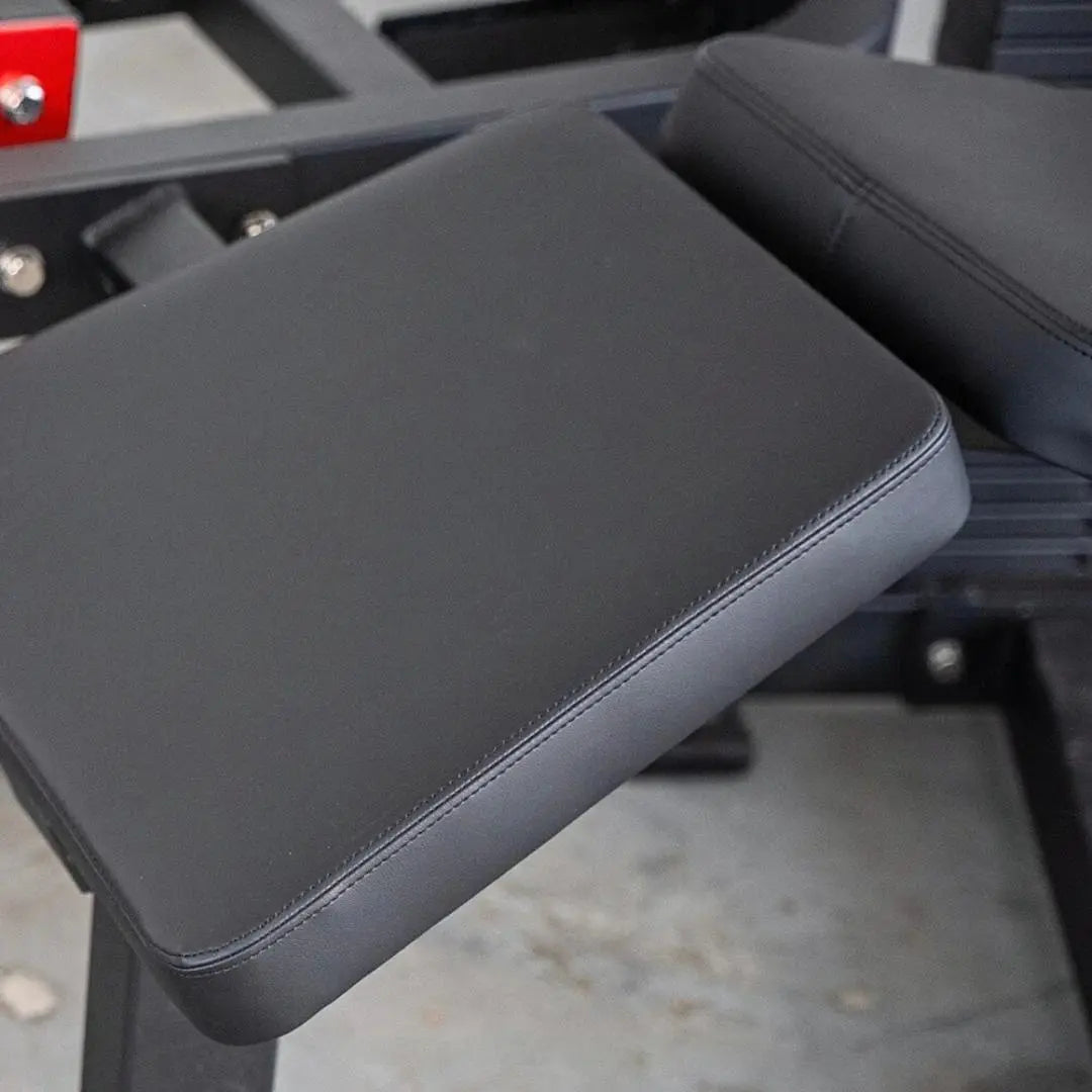 Black padded leg curl machine footpad with stitched seams and cushioned surface, part of a selectorized leg curl apparatus.