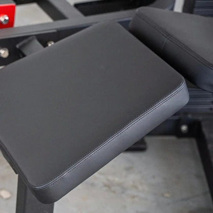 Black padded leg curl machine footpad with stitched seams and cushioned surface, part of a selectorized leg curl apparatus.
