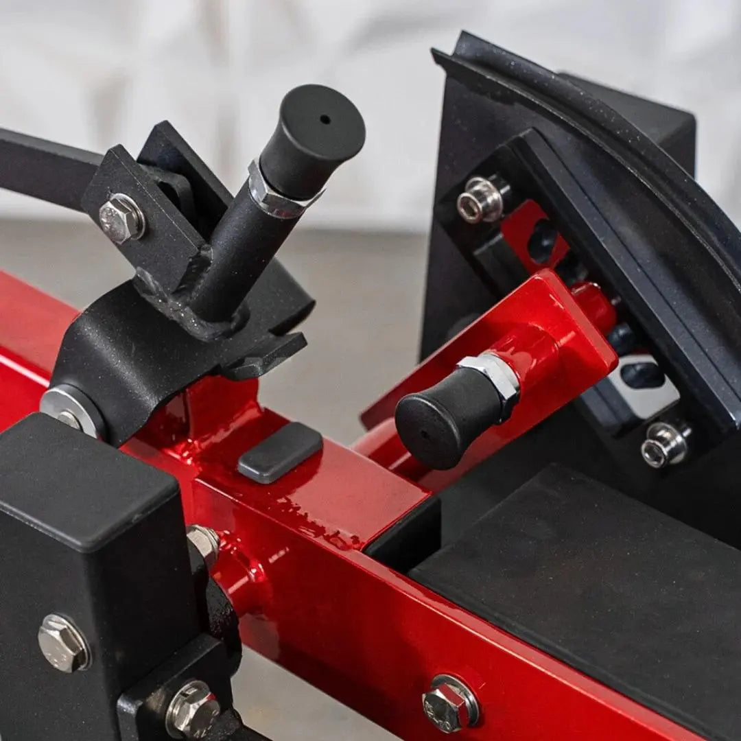 Close-up of selectorized prone leg curl machine showing red and black frame with adjustment knobs, footpad attachment, and metal fasteners.