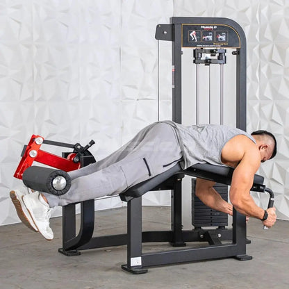 Man performing a leg curl exercise on a black and red selectorized leg curl machine with instruction graphics displayed on the upper panel.