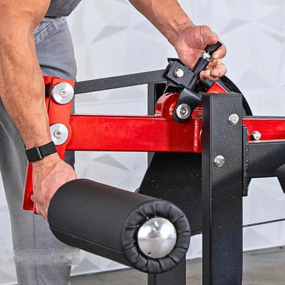 Man adjusting the pin on a red and black selectorized prone leg curl machine with padded leg roller and adjustment straps.