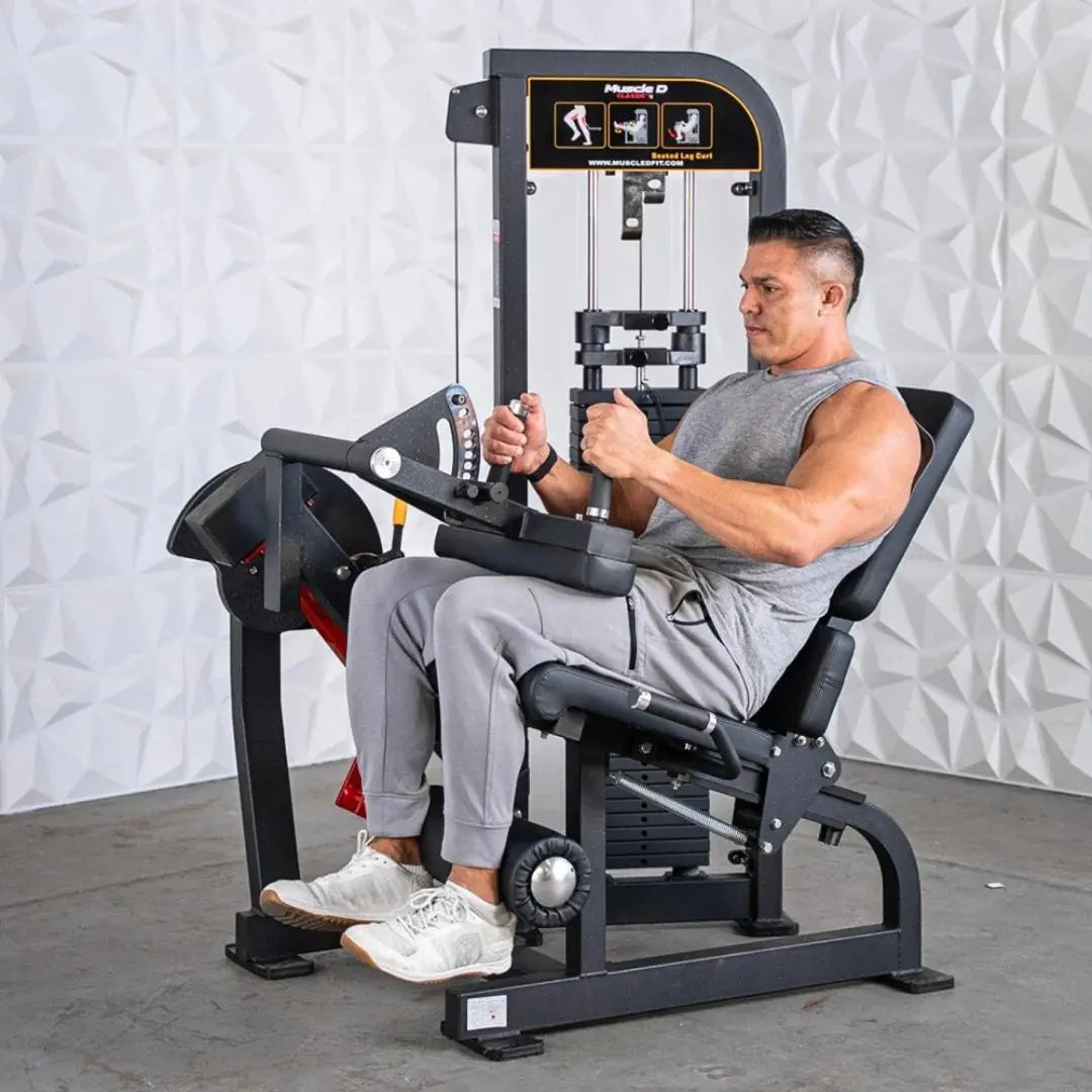 Man performing a seated leg curl on a black Muscle D Fitness selectorized machine with weight stack and instruction graphics on the upper panel.