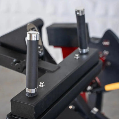 Close-up of adjustment pin with chrome and black cylindrical grip on a selectorized leg curl machine, with weight stack and red trim visible in the background.