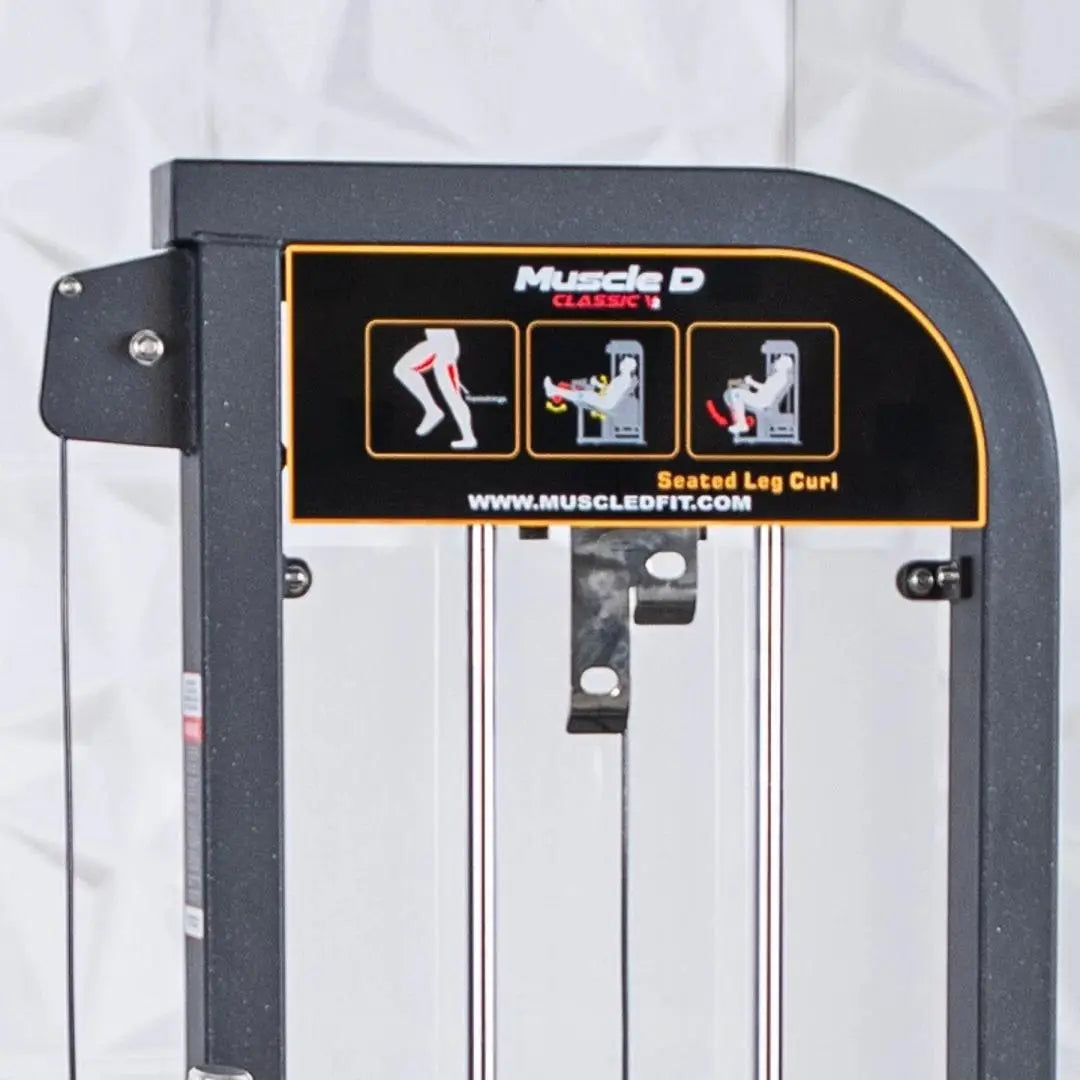 Muscle D Classic V2 selectorized seated leg curl machine with dark gray frame, white padded seat, and instruction diagrams on the backrest showing exercise form.