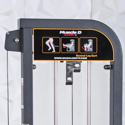 Muscle D Classic V2 selectorized seated leg curl machine with dark gray frame, white padded seat, and instruction diagrams on the backrest showing exercise form.