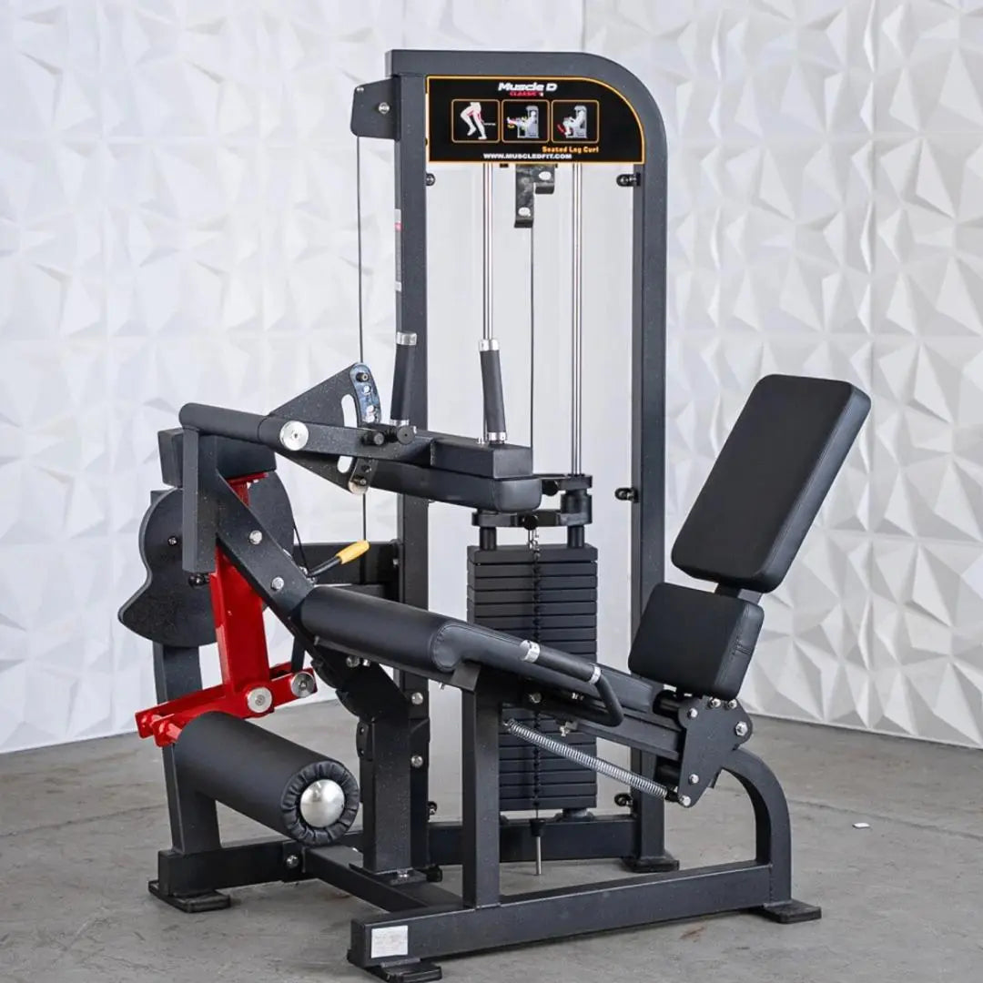 Black and red selectorized seated leg curl machine with padded seat and backrest, weight stack visible on side, instruction graphics on upper panel.
