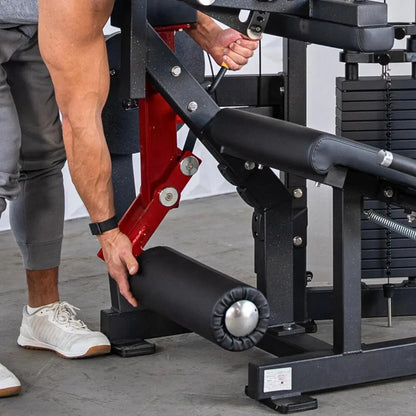 Man using a seated leg curl machine with black upholstery and red frame, adjusting the weight stack with his hand while seated.