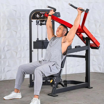 Man performing a shoulder press on a Muscle D selectorized machine with red arms and black frame in a gym setting.