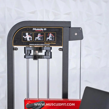 Muscle D Fitness Classic V2 selectorized shoulder press machine with black frame, red base, dual weight handles, and instructional diagrams on the backrest.