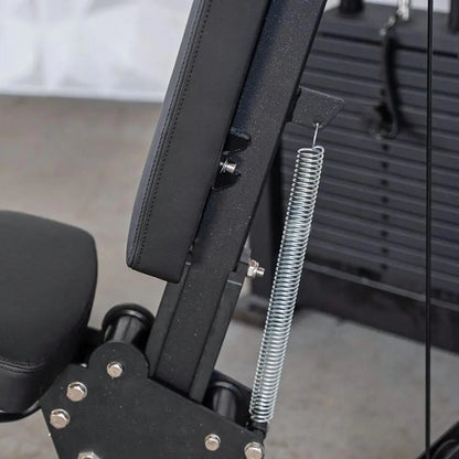 Close-up of shoulder press machine showing black padded seat back, adjustment lever, and silver coiled spring mechanism on the frame.