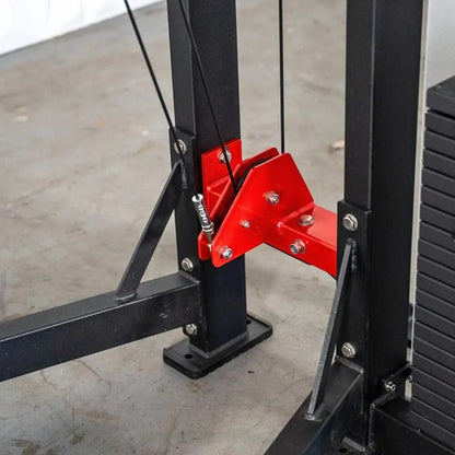 Black power rack with red V-shaped foot platform and attached cables for standing calf raise exercise. Machine features bolt connections and is positioned on concrete gym flooring.