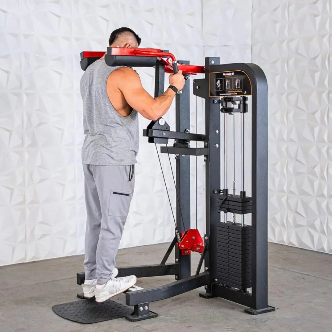Man performing calf raise on a black and red selectorized standing calf raise machine with weight stack, against a white textured backdrop.