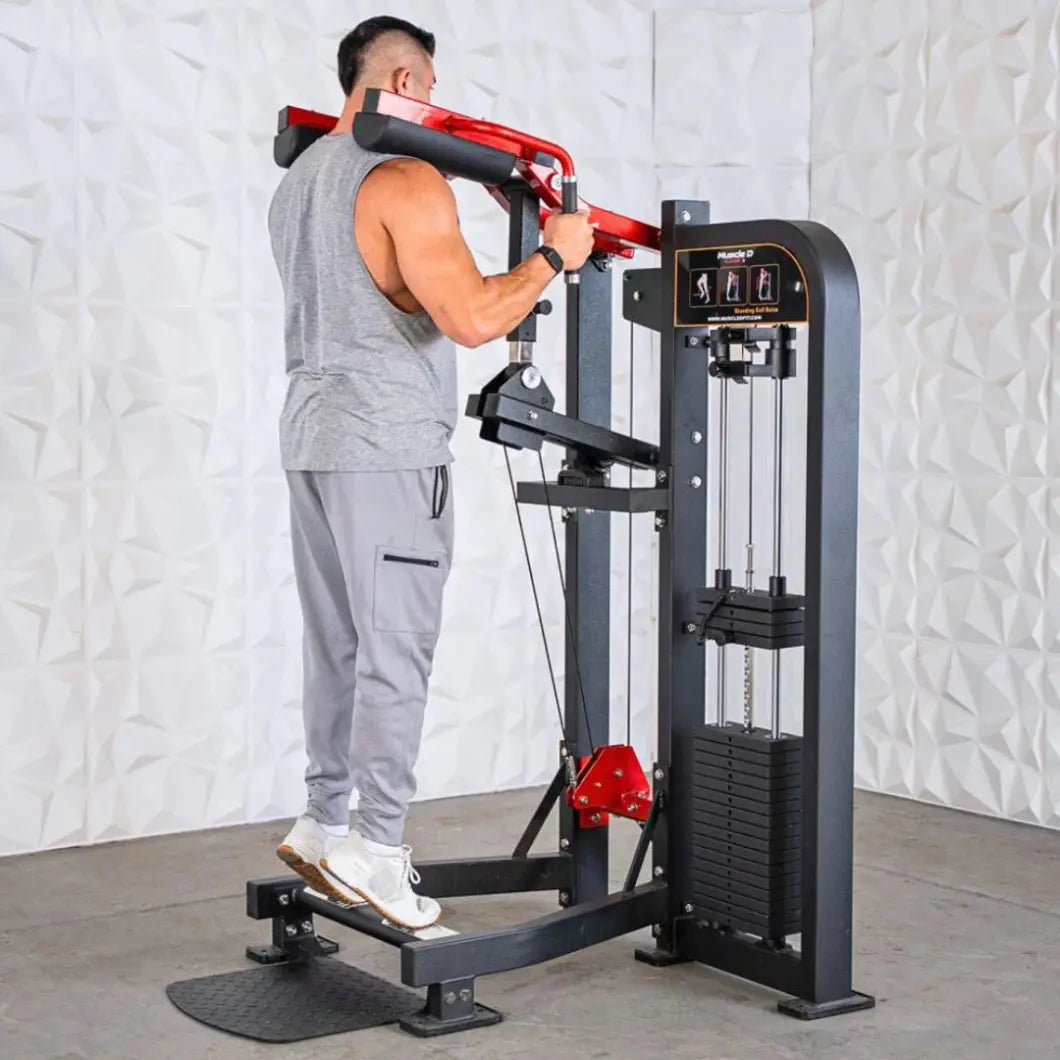 Man performing standing calf raise on a black and red selectorized machine with weight stack and padded shoulder supports in a gym setting.