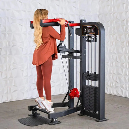 Woman performing a standing calf raise on a black selectorized machine with red handles and black footplate, against a white textured wall.