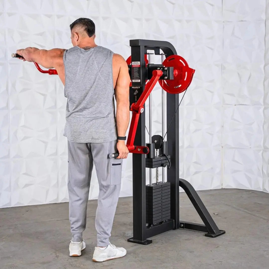 Man performing a lateral raise on a selectorized machine with red handles and black frame against a white brick wall.