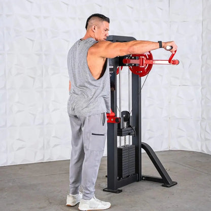Man performing a lateral raise on a selectorized machine with red handles and black frame against a white brick wall.