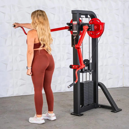 Woman performing a lateral raise on a standing shoulder machine with a red arm and black frame equipped with a red weight plate.