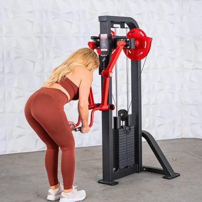 Woman performing a lateral raise on a selectorized machine with a black frame, red handles, and red weight plate, against a white brick wall.