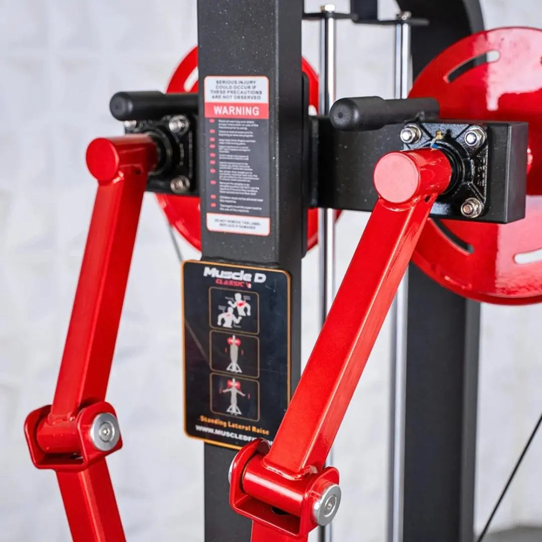 Red and black selectorized standing lateral raise machine with dual arm handles, weight stack, and instruction decals on the black frame.