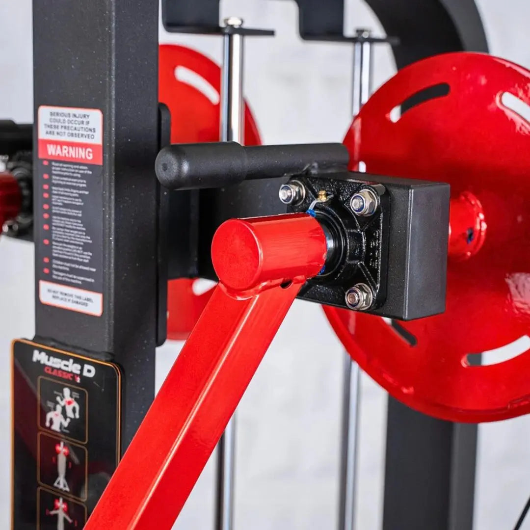 Close-up of the lever mechanism on a selectorized standing lateral raise machine with red handles, black frame, and warning label visible on the side.