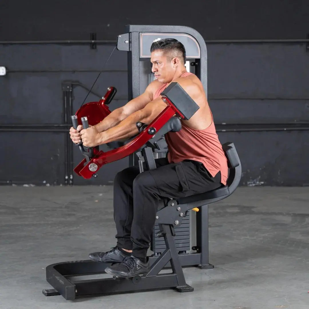 Man performing triceps extension on a selectorized machine with red arms and gray padding in a gym setting.