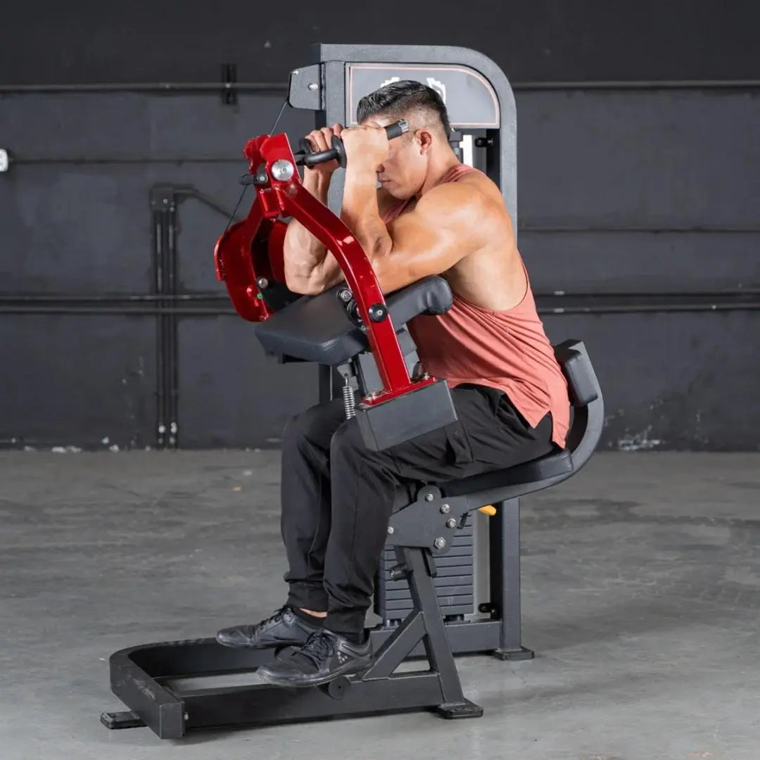 Man performing triceps extension on a red and black selectorized machine with adjustable arm lever in a gym setting.