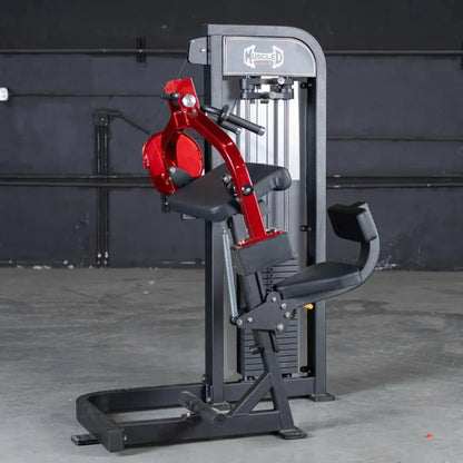 Commercial selectorized triceps extension machine with gray frame, red upper arm attachment, and black seat and footrest in a gym setting.