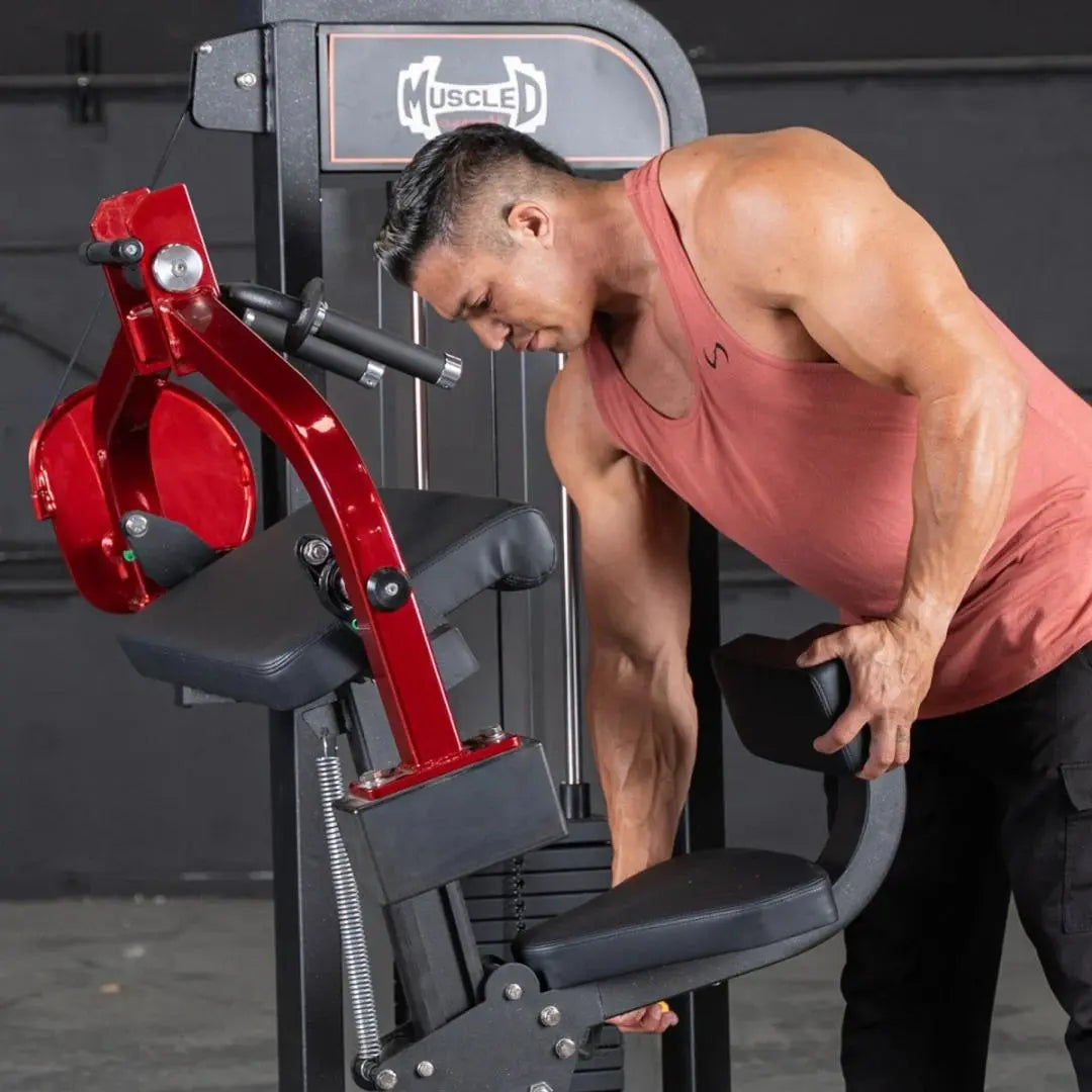 Man performing triceps extension on a selectorized Muscle D Fitness machine with red arm lever and black seat in a gym setting.