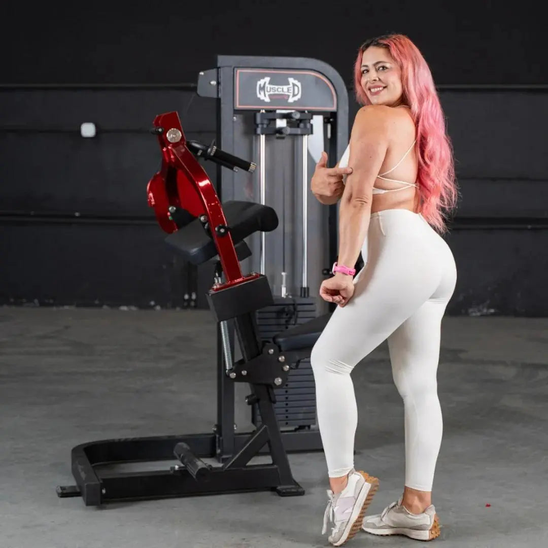 Woman using a Muscle D selectorized triceps extension machine with red lever arms and black frame in a gym setting.