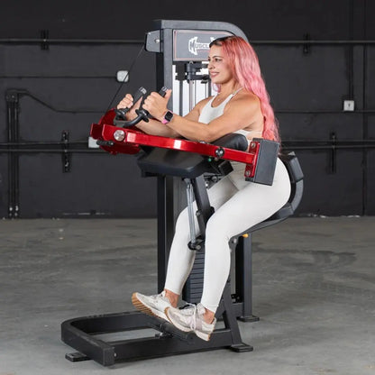 Woman performing triceps extension on a commercial selectorized machine with red arms and black frame in a gym setting.